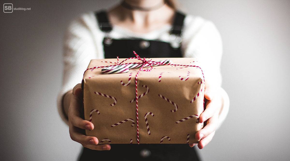 Geschenktipps für Weihnachten für Studenten: Studentin hält ein Päckchen mit Zuckerstangen in die Kamera