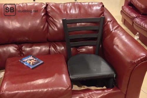 Auf einer roten Couch wurde ein Sitzplatz durch einen schwarzen Holzstuhl "repariert" - Dinge, die arme Studenten machen.